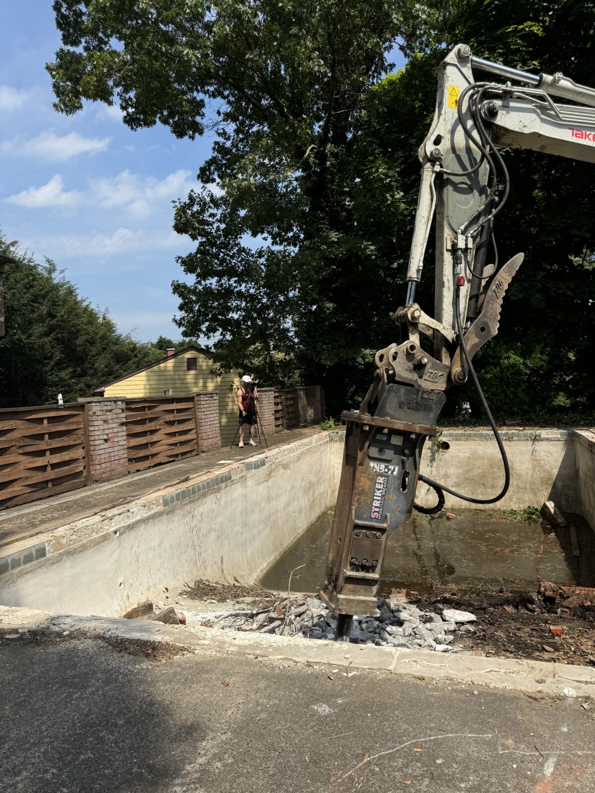 Hydraulic breaker hammer demolishing thick concrete pool shell in Connecticut