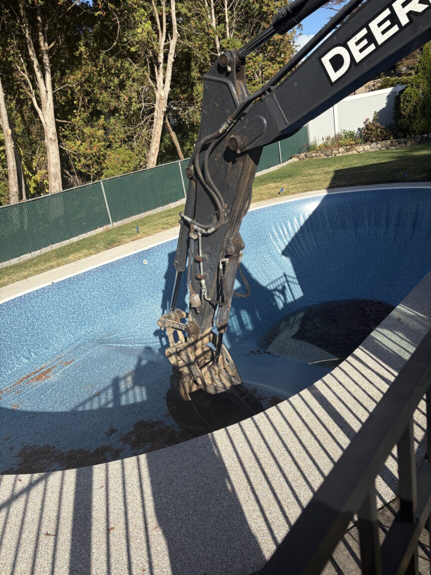 Excavator bucket inside a drained vinyl liner inground pool in Stratford CT, beginning the demolition and removal process